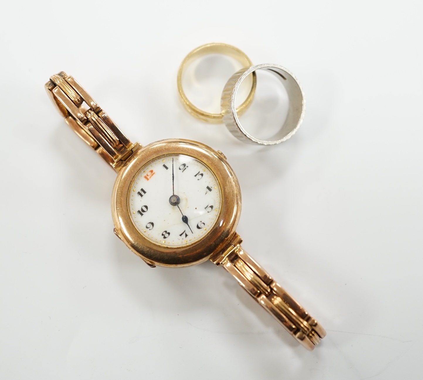A textured white metal (stamped platinum) band, 7 grams, an 18ct gold band,4.5 grams and a 9ct gold manual wind wrist watch, on a 9ct expanding bracelet, gross weight 23 grams.